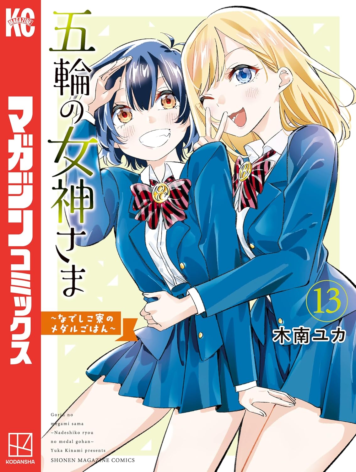 『五輪の女神さま ～なでしこ寮のメダルごはん～』13巻の表紙イラスト。青い制服姿の少女2人が並んで描かれており、金髪の少女がウインクしながらピースサインを見せ、黒髪の少女は笑顔で敬礼ポーズを取っている。仲の良さを感じさせる明るい雰囲気のデザイン。